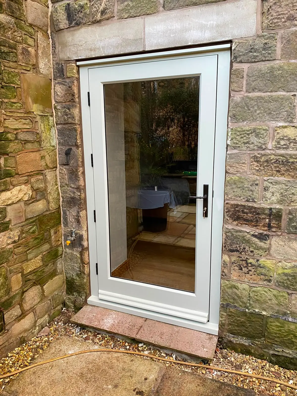 Fully glazed external door in painted timber, hung in a new frame within a sandstone opening, with a weathered cill and lever handle.
