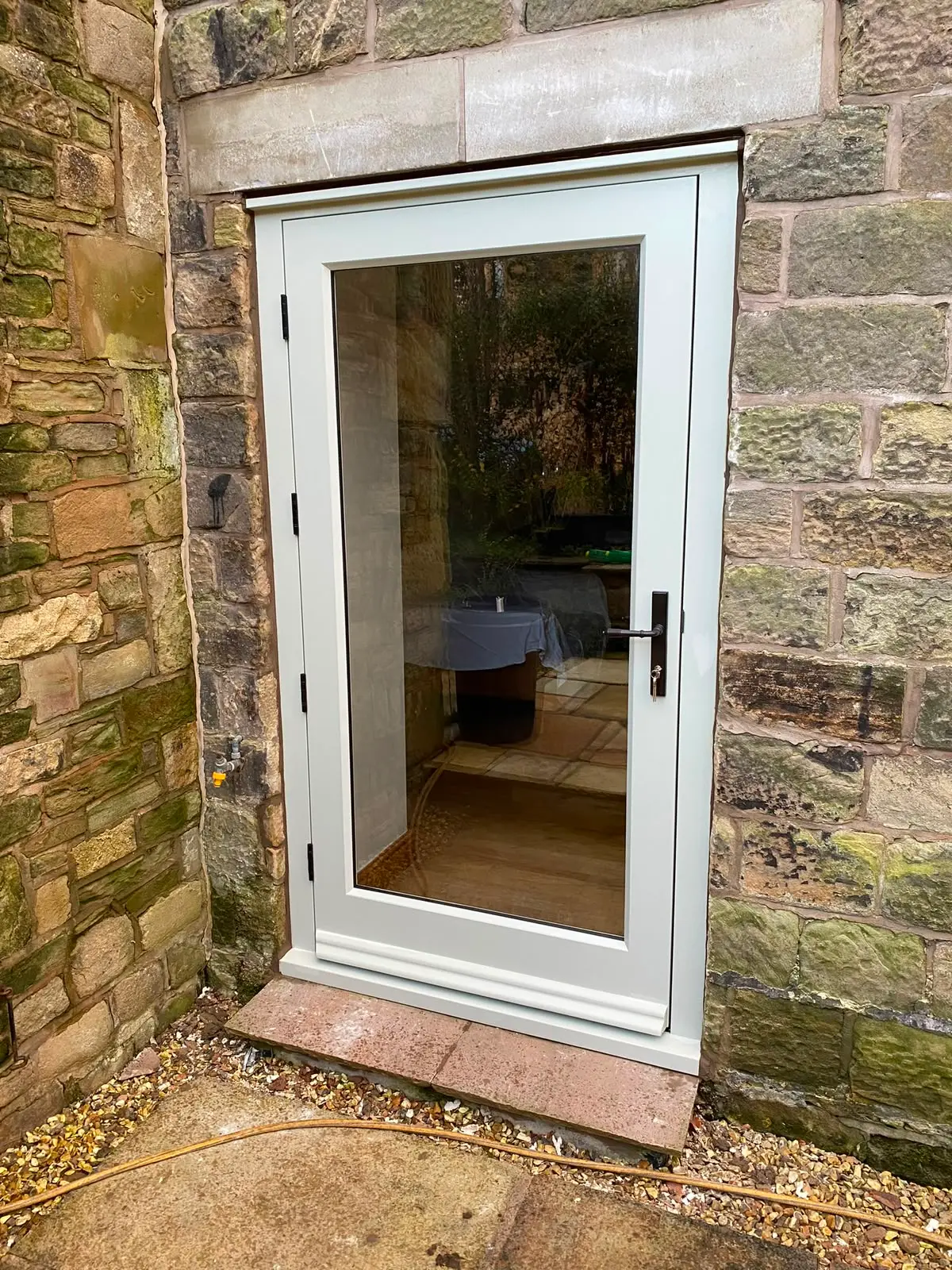 Fully glazed external door in painted timber, hung in a new frame within a sandstone opening, with a weathered cill and lever handle.