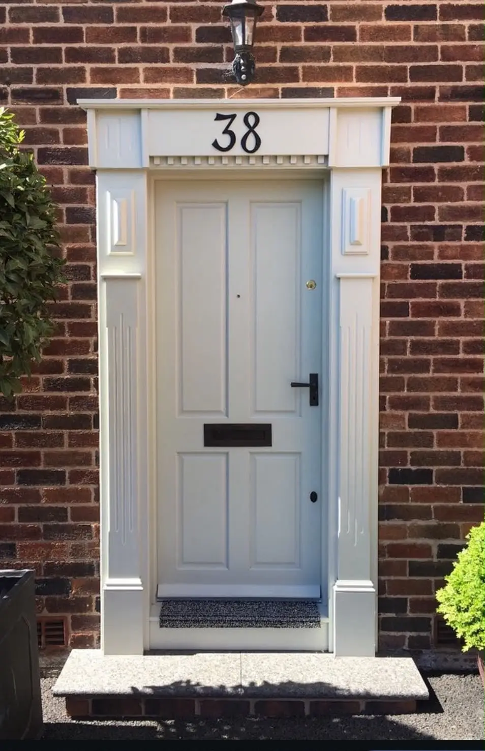 Cream painted front door with six raised panels and a polished letterplate, framed by fluted pilasters and a dentil-moulded pediment carrying the house number.