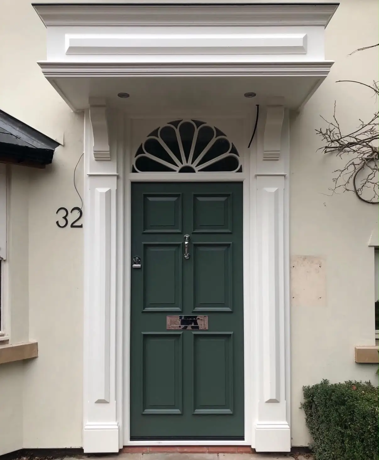 Georgian style front door painted dark green with six raised panels, set beneath a semicircular fanlight with radiating glazing bars, between fluted pilasters and a moulded portico.