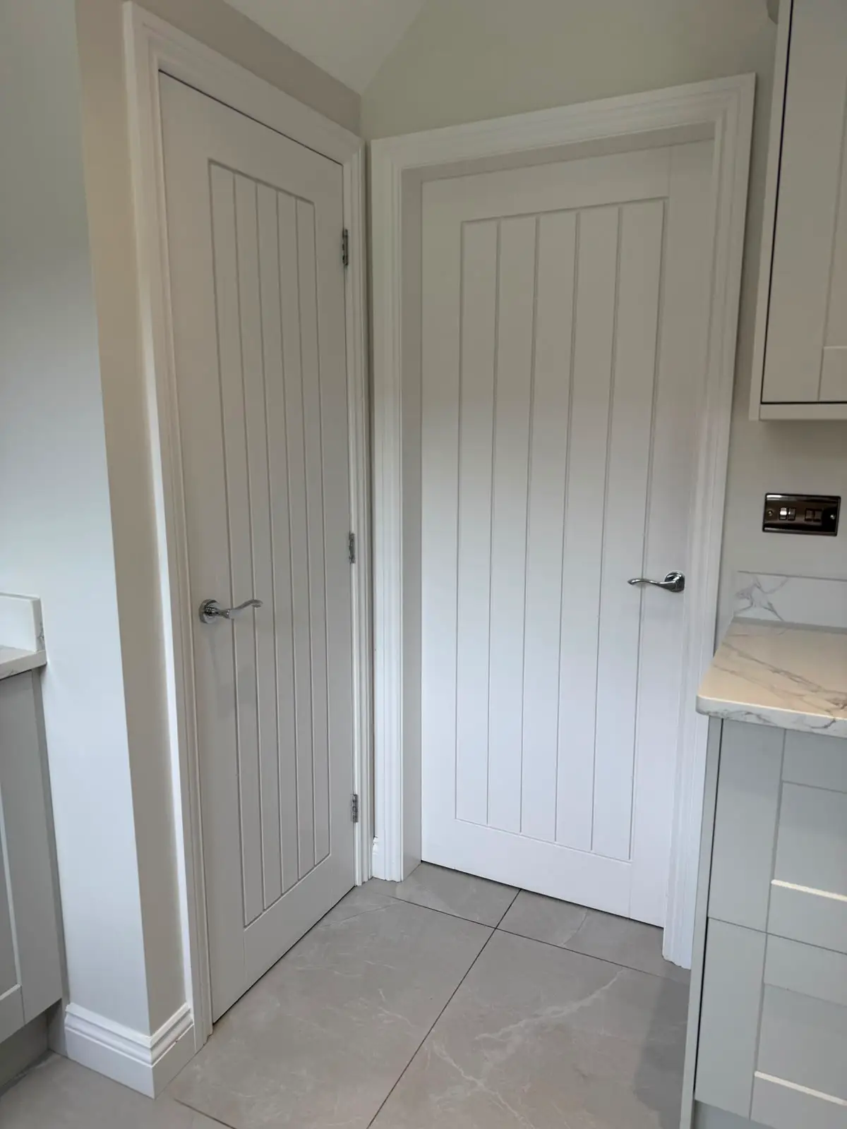Two white boarded doors hung in adjacent openings off a utility area, each in a new lining with moulded architrave and chrome lever handles.