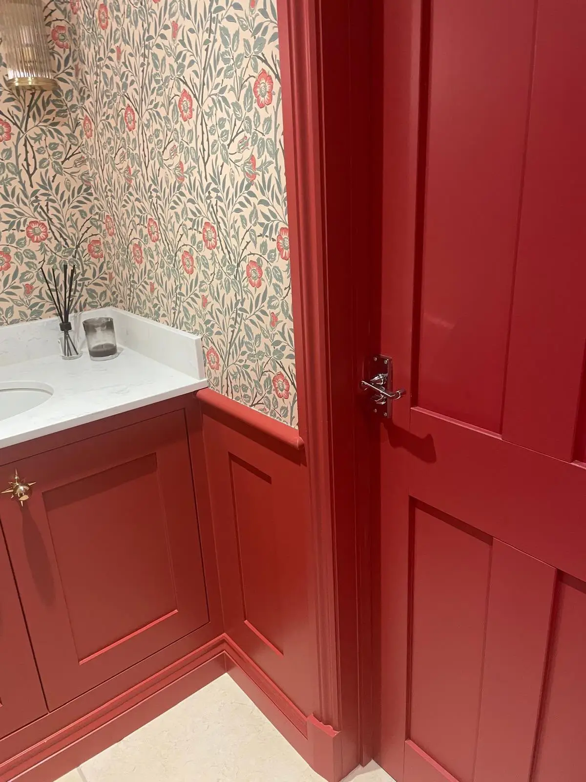 The same red cloakroom seen wider, the vanity carrying through to matching panelling and a boarded door hung on a thumb latch.