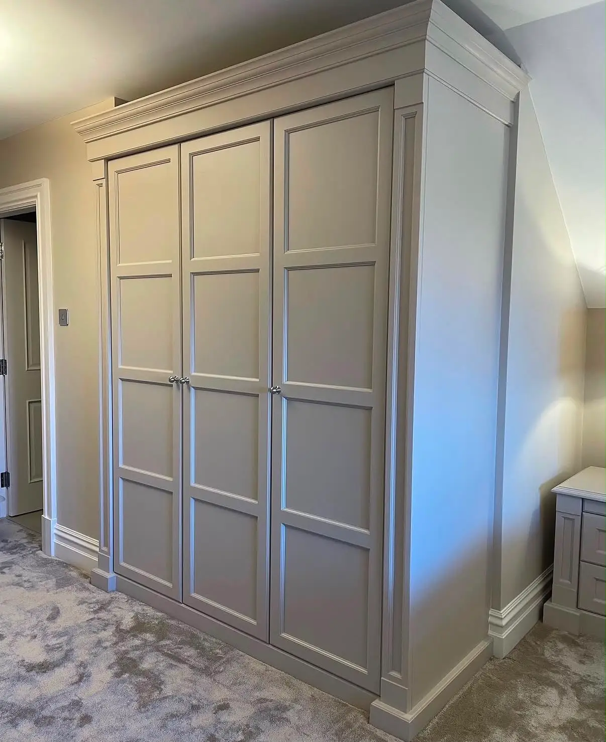 Grey painted fitted wardrobe built into a room with sloping eaves, with panelled doors and a moulded cornice.