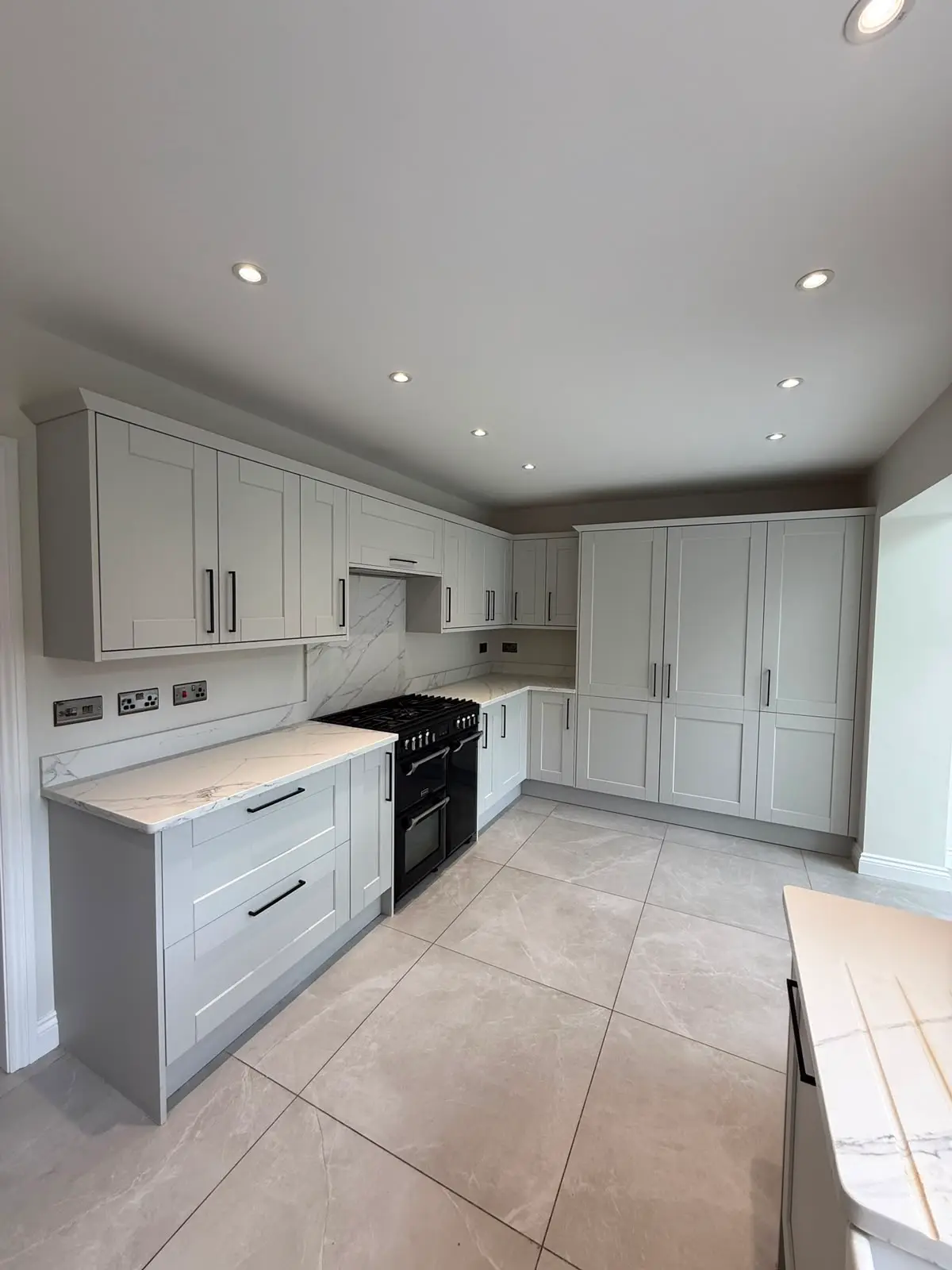 Light grey shaker kitchen with marble-effect worktops and upstand, a black range cooker and full-height cabinetry.