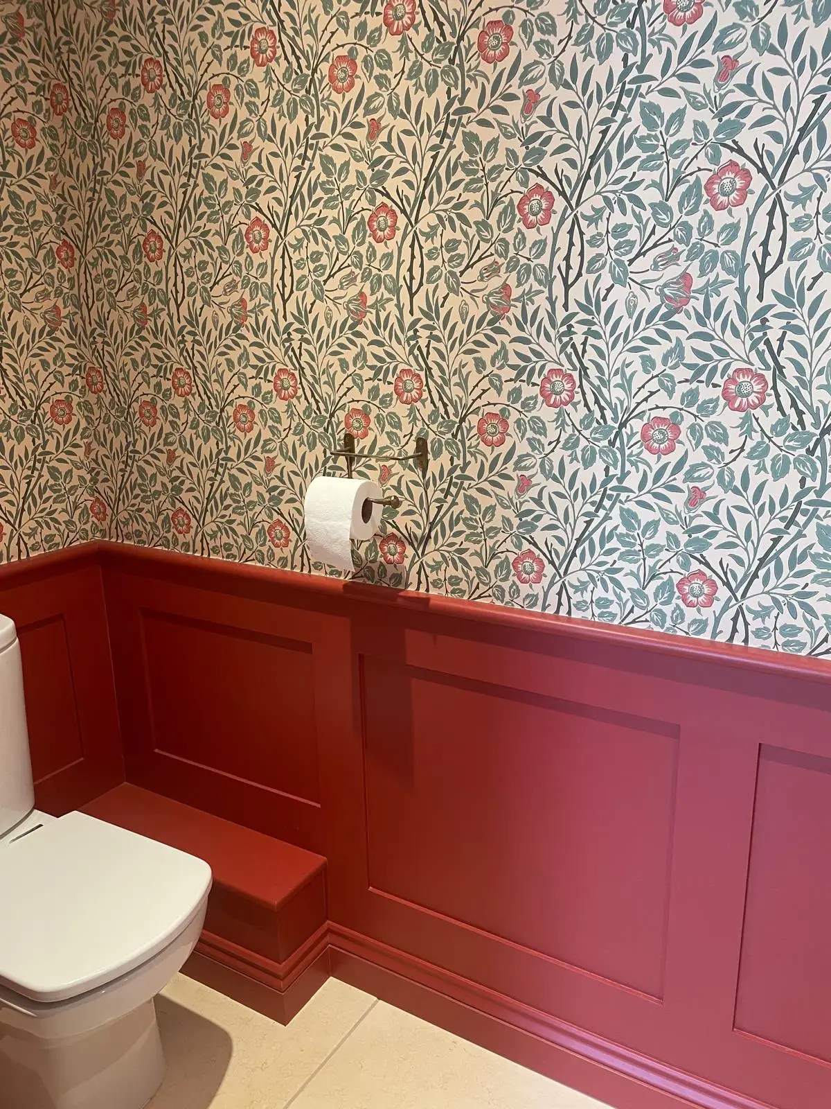 Deep red panelling to dado height in a cloakroom, with a moulded capping rail, beneath patterned floral wallpaper.