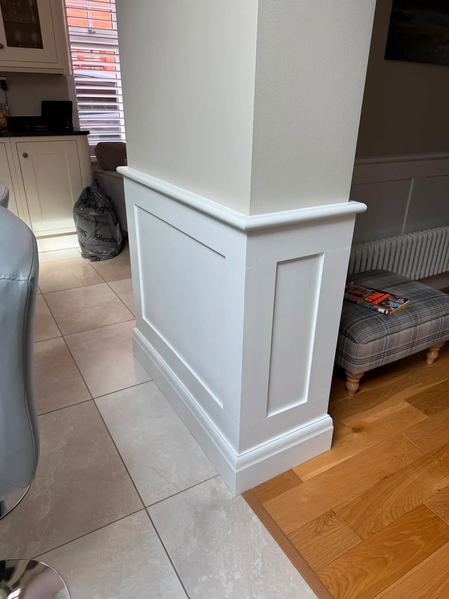 A structural column cased in white panelling with a moulded cap and skirting, squaring the pillar into the room.