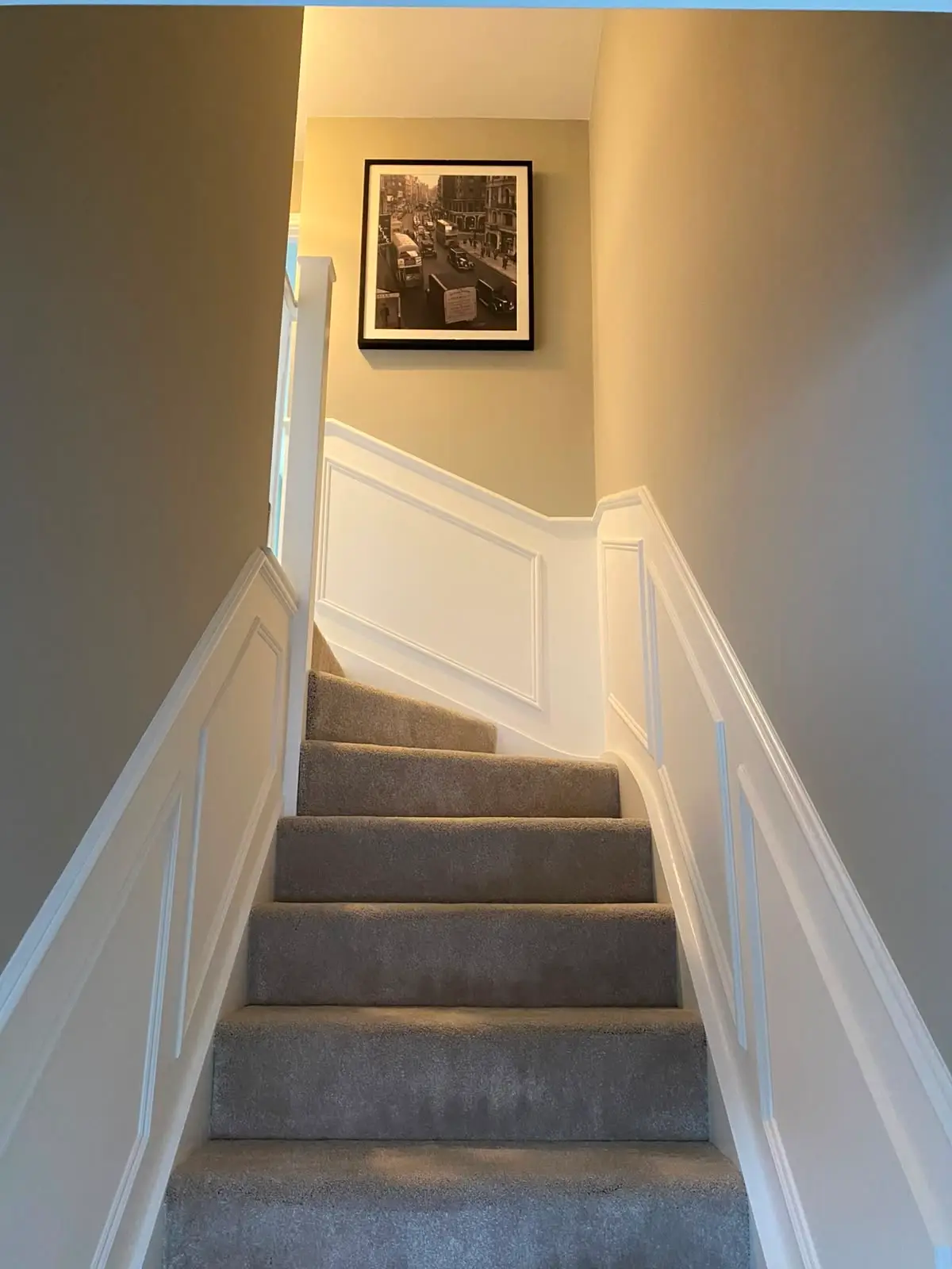 White panelling running up a staircase wall, its rail stepping with the flight and returning level along the landing, beside turned spindles and a newel post.