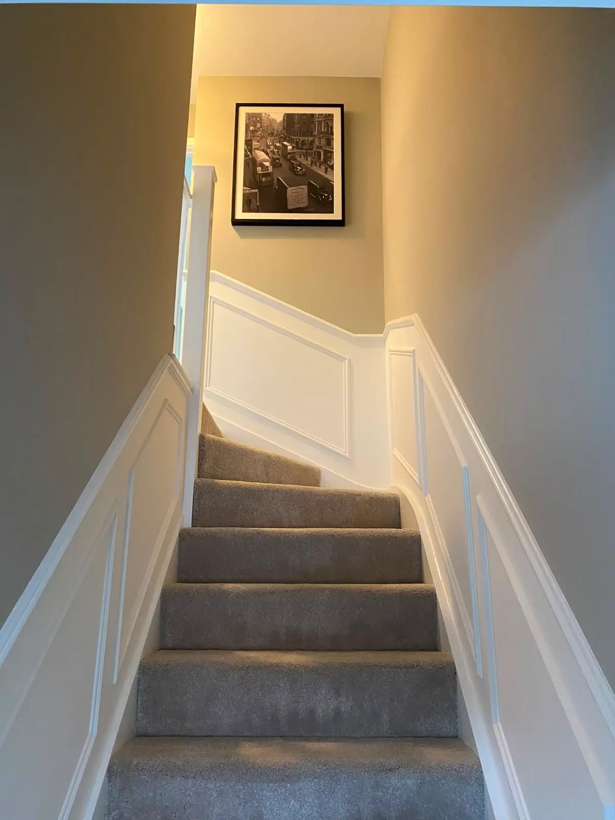 White panelling running up a staircase wall, its rail stepping with the flight and returning level along the landing, beside turned spindles and a newel post.