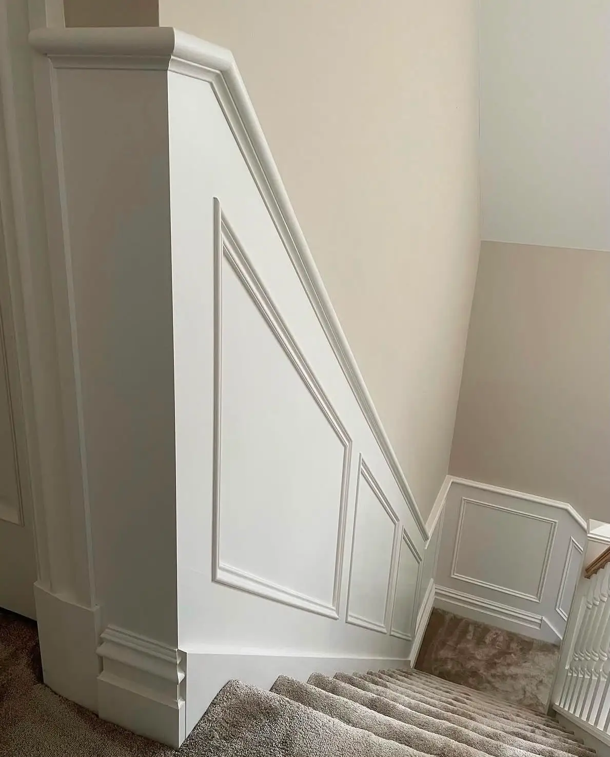 Understair elevation panelled in white, the mouldings raked to follow the underside of the flight and meeting a moulded skirting at the floor.