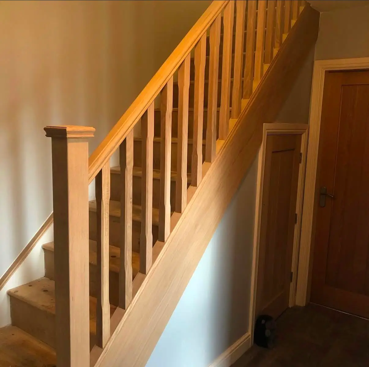 Oak staircase mid-installation, showing the newel post, moulded handrail and shaped spindles above bare timber treads.