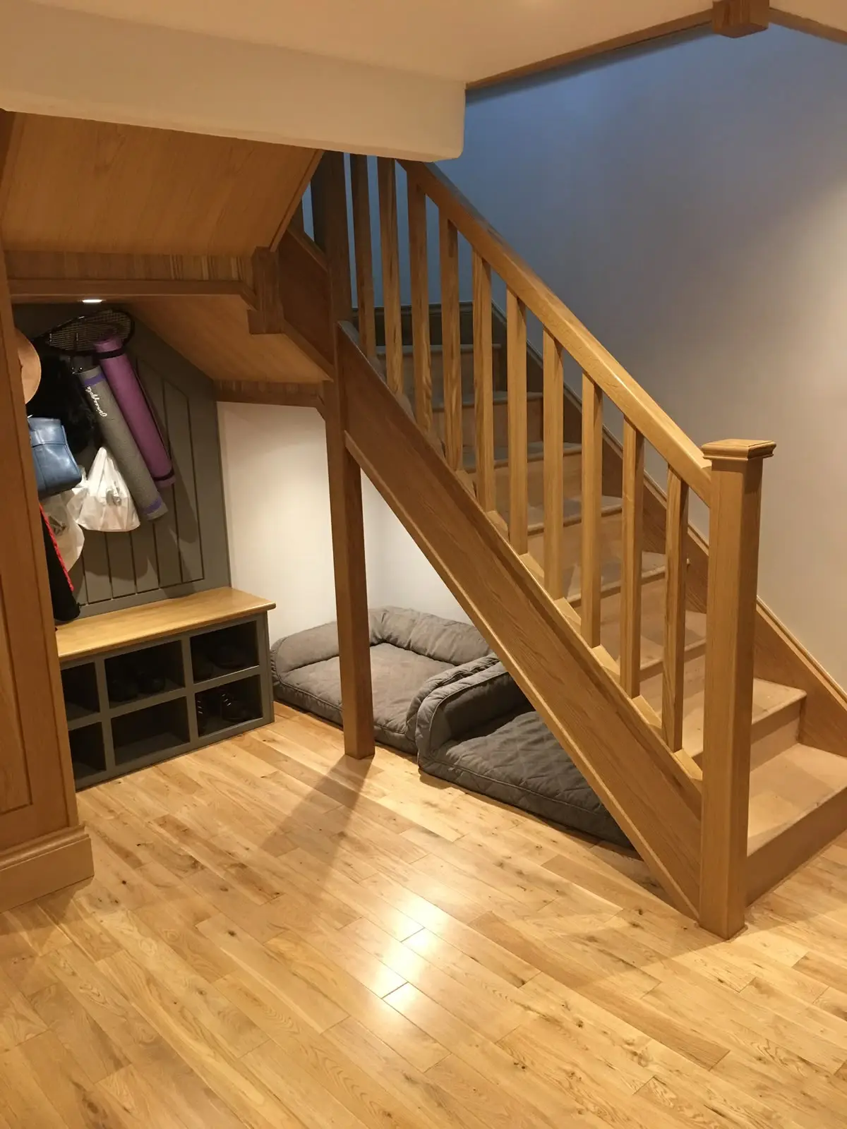Understair storage nook with a fitted oak bench, cubby shelving and boarded panelling to the back wall.