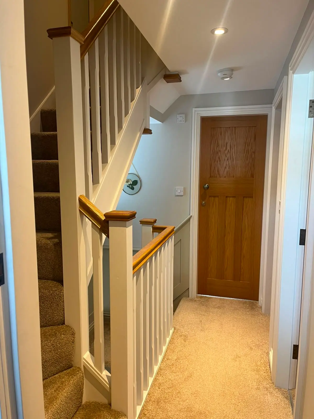 Painted staircase and landing balustrade with oak capping to the handrail and newels, in a hallway with an oak four-panel door.