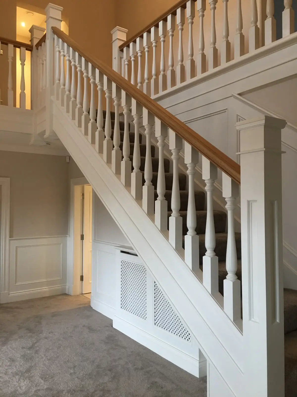 Painted staircase with turned balusters and an oak handrail rising to a galleried landing, over a fretwork radiator cover set into the understair panelling.