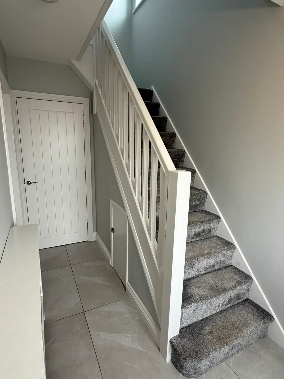 Panelled understair elevation in white, with a concealed access door set flush into the panelling.