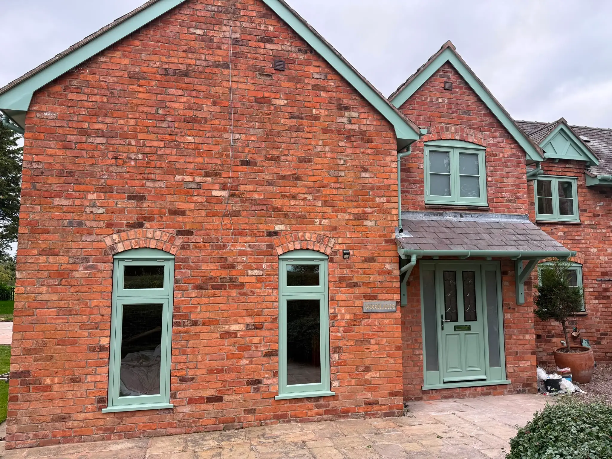 Sage green casement windows across the front of a red brick house, with brick arches over the openings and a matching porch and door surround.