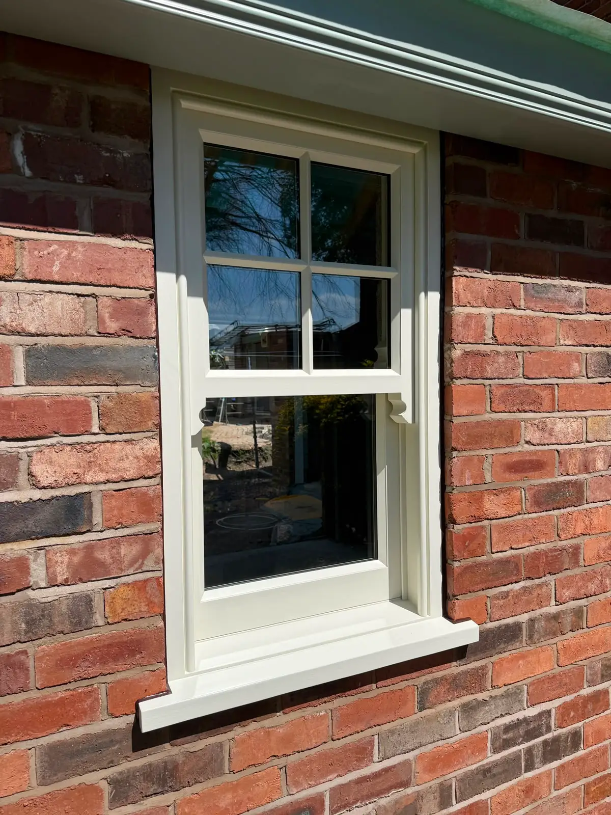 Cream painted sash window with glazing bars to the upper sash and shaped horns, set into new red brick above a moulded timber cill.