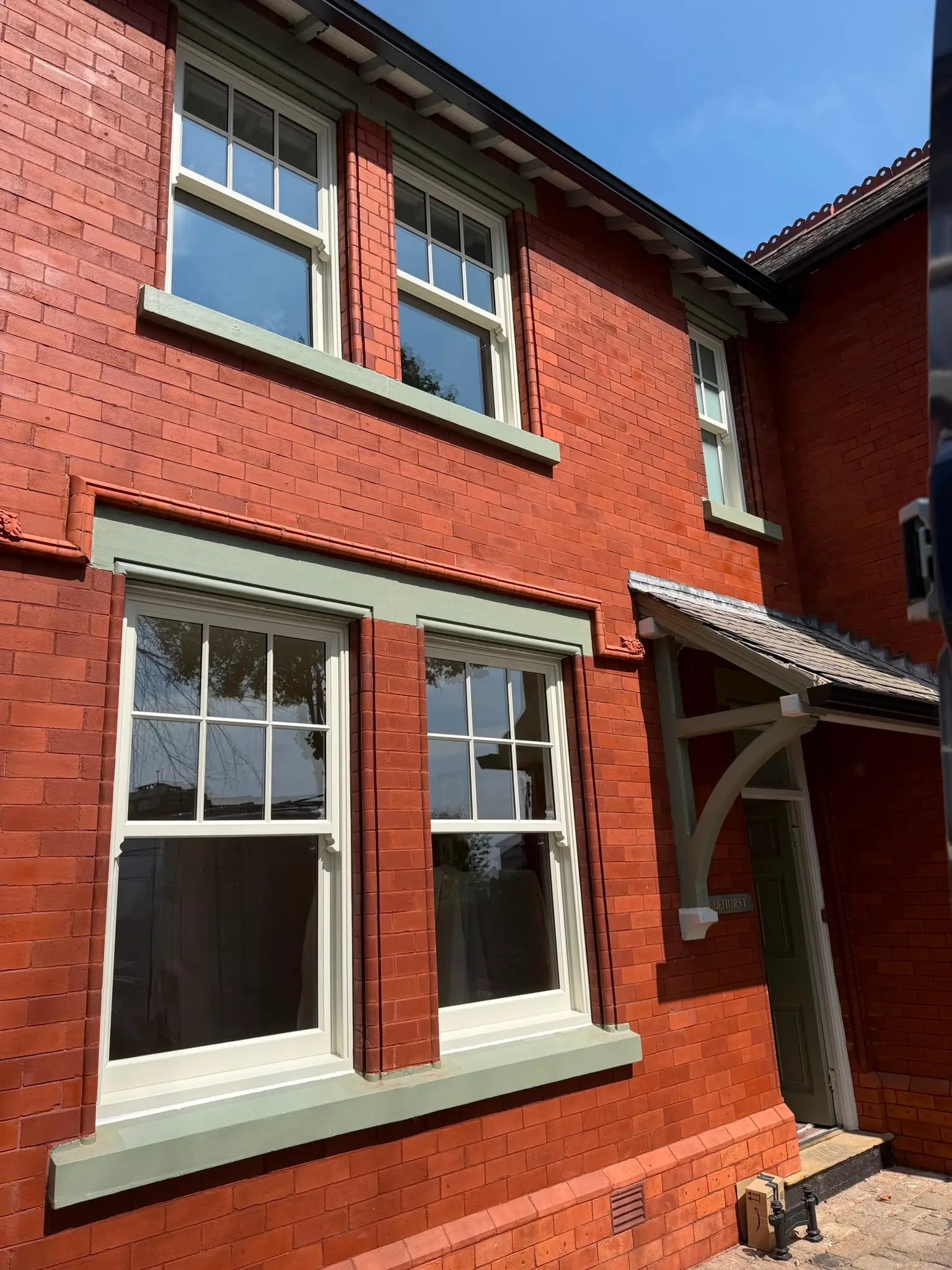 Sash windows across two storeys of a red brick house, with painted sills, heads and a timber porch bracket.