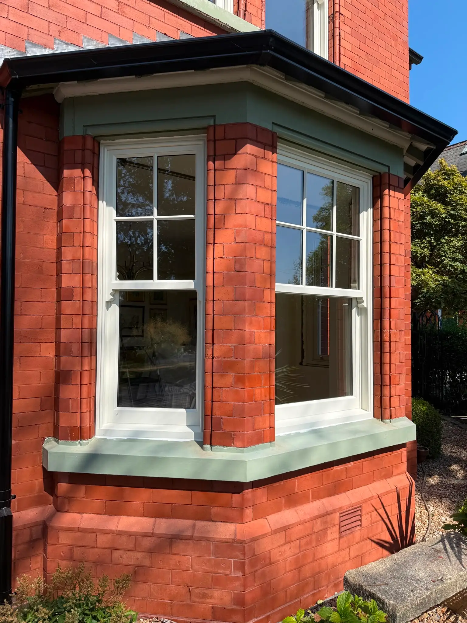 White timber sash windows in a splayed bay, set into red brick with a painted sill and moulded head.