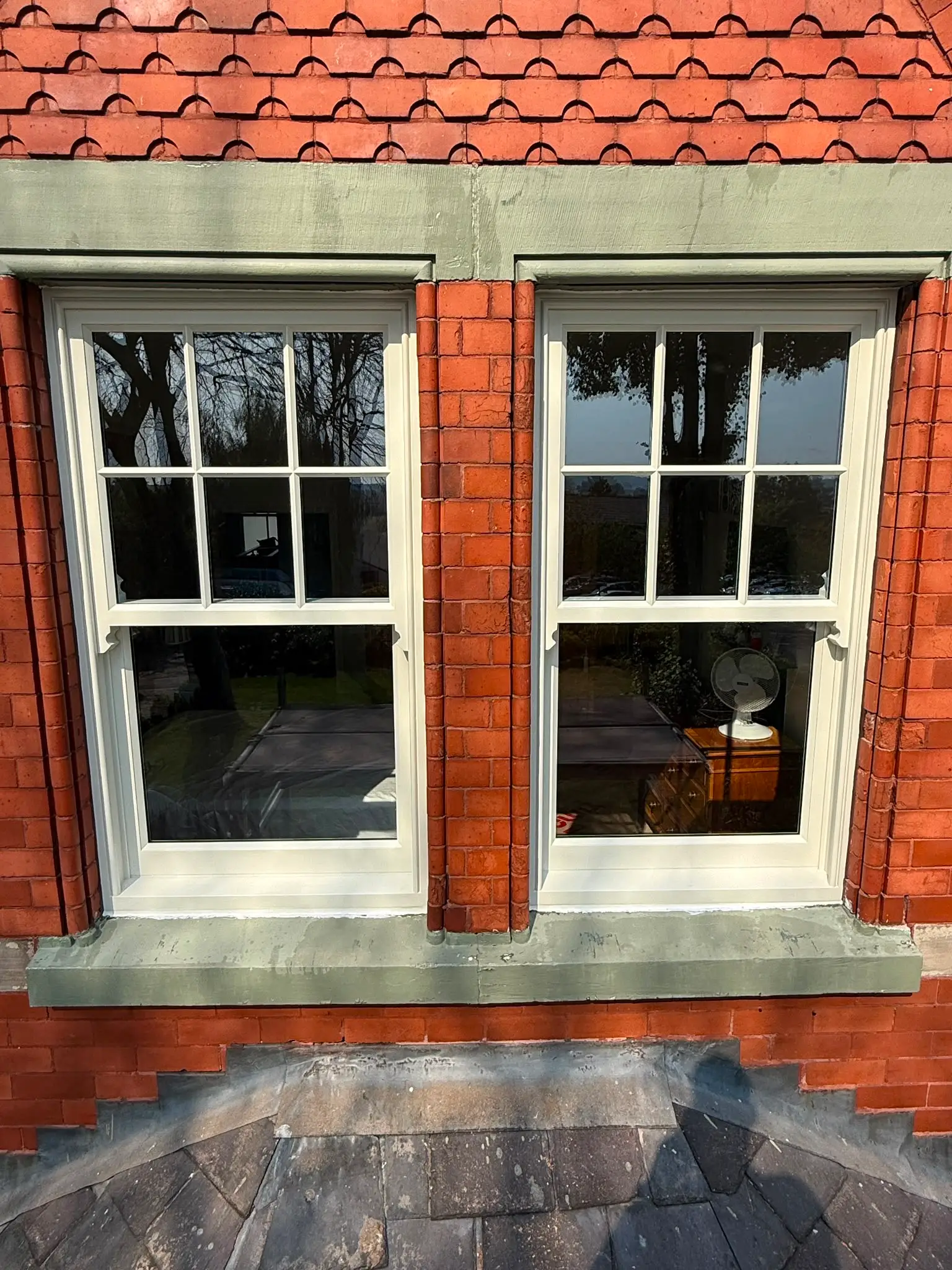 Pair of white timber sash windows with glazing bars, sharing a painted stone sill on a red brick elevation.